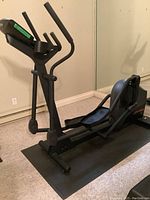 Side perspective of elliptical on protective mat showing entire frame, handles, pedals and console