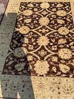 Full view of the rectangular area rug showing the dark brown background with beige floral motifs and light beige floral border.