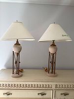 Pair of table lamps standing 30 inches tall on a dresser with beige and gold metal bases and white fabric shades.