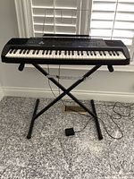 Full view of keyboard mounted on X-style stand with music rest attached, AC adapter and sustain pedal visible
