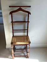 Front view of the vintage wooden valet stand showing hanger, horizontal bars, and woven seat.