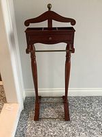 Full front view of the wood valet stand showing the hanger top, drawer, and base with towel bar.