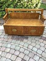 Full view of wooden storage bench with armrests, back rest, and drawers visible, placed on a paved outdoor surface.