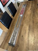 Curtain rod set in unopened clear packaging lying on a wooden table showing full length of rod and decorative ends.