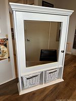 Front view of the white bathroom cabinet showing mirrored door and two wicker baskets below