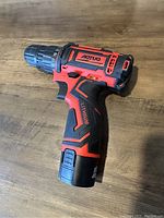Photo of the cordless drill showing red and black body with torque settings on the chuck and AOTUO branding.