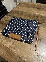 Laptop case displayed closed on wooden table showing front with polka dot pattern and leather details.