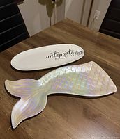 Both mermaid tail resin platter and white porcelain antipasto platter displayed on wooden table.