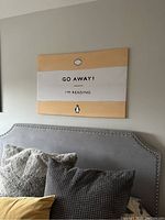 Framed stretched fabric piece hung on wall above bed headboard showing text and design.