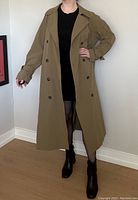 Front view of a camel brown trench coat worn over a black dress, showing open front with button details and relaxed fit.