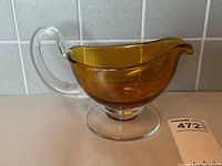 Side view of the amber glass gravy boat showing clear handle and base, highlighting the smooth glass finish and amber color.