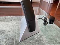 Front angle of Beocom 6000 black cordless phone on silver triangular base with power adapter beside it, showing overall lot.