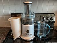 Silver and black Breville Juice Fountain Juicer with a clear juice container and white pulp container on a kitchen counter.