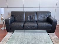 Full front view of black leather sofa in living space with glass coffee table.
