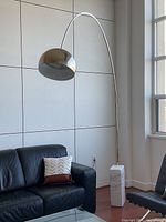 Full view of lamp positioned by sofa showing curved chrome stem and dome shade