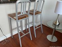 Pair of bar stools side by side showing wooden seats and aluminum frames against wall