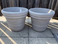 Photo of two large light gray planters with cement-like finish showing front view outdoors on stone surface.