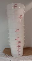 Stacked white plastic pails showing side with red measurement markings up to 15 liters and 4 gallons, handles visible