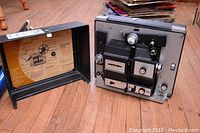 Photo showing the Bell and Howell compatible 8mm Super 8 projector beside its open carrying case showing instruction sheet inside.