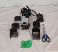 Photo showing Andis electric hair trimmer with 6 black attachment combs and blue-handled scissors arranged on a white surface