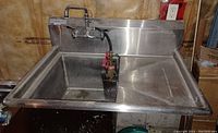 Front view of commercial stainless steel sink showing basin, faucet, and clean-in-place dispenser inside basin.