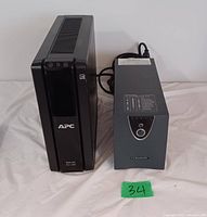 Photo of two UPS units, one APC Pro 1300 on the left and one Powervar UPS on the right, placed on a white surface with a green label '34'.