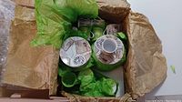 Set of espresso cups and saucers wrapped partially in green tissue and brown packing paper inside a box.
