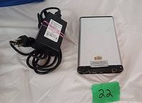 Silver 3.5 inch external hard drive enclosure with black ends. Includes power adapter with EU plug and USB cable coiled beside it on white background.