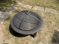 Top-down view of the fire pit with grill and lock attached on grill surface, showing the fire pit bowl and legs.