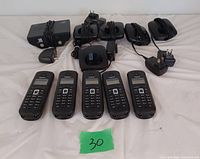 Five black Gigaset cordless handsets laid out with charging cradles and multiple power adapters on a white background.