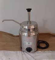 Heated liquid dispenser unit with thermostat dial and attached power cord, showing the outside and top pump dispenser.