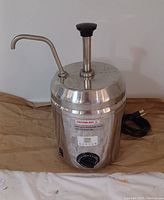 Closed unit showing stainless steel body, power cord, temperature dial, and dispensing spout with pump.