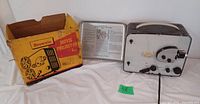 Photo of Kodak Brownie Model 2 movie projector with original yellow/red box and removable-sided carrying case with instructions.