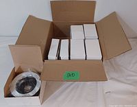 Open box showing multiple white boxes each containing a pot light bezel, with one bezel visible wrapped in plastic.