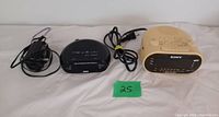 Photo of two digital clock radios, black RCA and beige Sony, both with power cords visible.