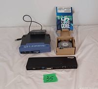 Photo shows three distinct items: a Linksys Ethernet switch, a laptop docking station, and an Intel Core i5 cooling fan with heatsink inside an open box.