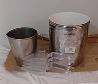 Photo of two metal serving containers and four clear plastic scoops arranged in front of them on a neutral background.