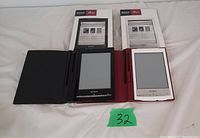 Two Sony e-readers side-by-side on a white background, one black with a black case and one white with a red case, both accompanied by instruction manuals.
