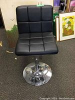 Front view showing padded, square tufted black vinyl seat and backrest, chrome round base and footrest ring.