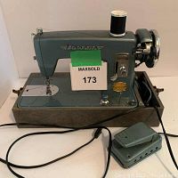 Front and side view of the vintage Brother Dorcas sewing machine with foot pedal and cord attached, spool of thread placed on top