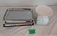Both vintage kitchen scales side by side against a wall, one green with round white plate, one rectangular Soehnle scale with metal tray.