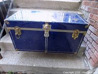 Closed blue vintage trunk showing brass corner protectors and latches on a stair surface