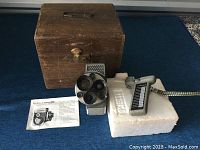 Full setup showing wooden box, Yashica camera with turret lenses, accessory control on styrofoam, and instruction manual on blue fabric.