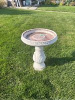 Full view of the concrete bird bath placed on grass showing its round basin with Greek key border design and decorative pedestal.