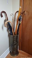 Photo shows a brass umbrella stand holding several canes and umbrellas displayed upright.