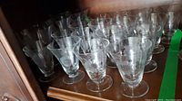 Group of clear stemmed liquor glasses with etched cornflower design on a wooden shelf.