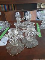 Five clear glass candle holders with cornflower design sitting on table, showing double-arm holders in front.