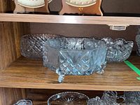Three crystal serving bowls displayed on a wooden shelf showing their cut glass patterns and shapes.