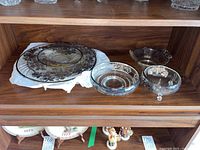 Multiple glass platters and candy dishes displayed on a wooden shelf, all featuring silver overlays.