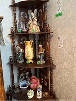 Wide view of wooden corner shelf holding various figurines, vases, and decorative items with green lot stickers.